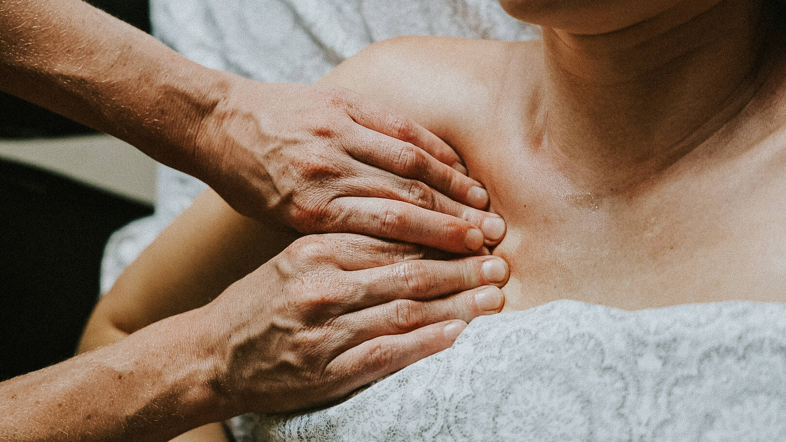 Woman laying on massage bed with two hands massaging her shoulder